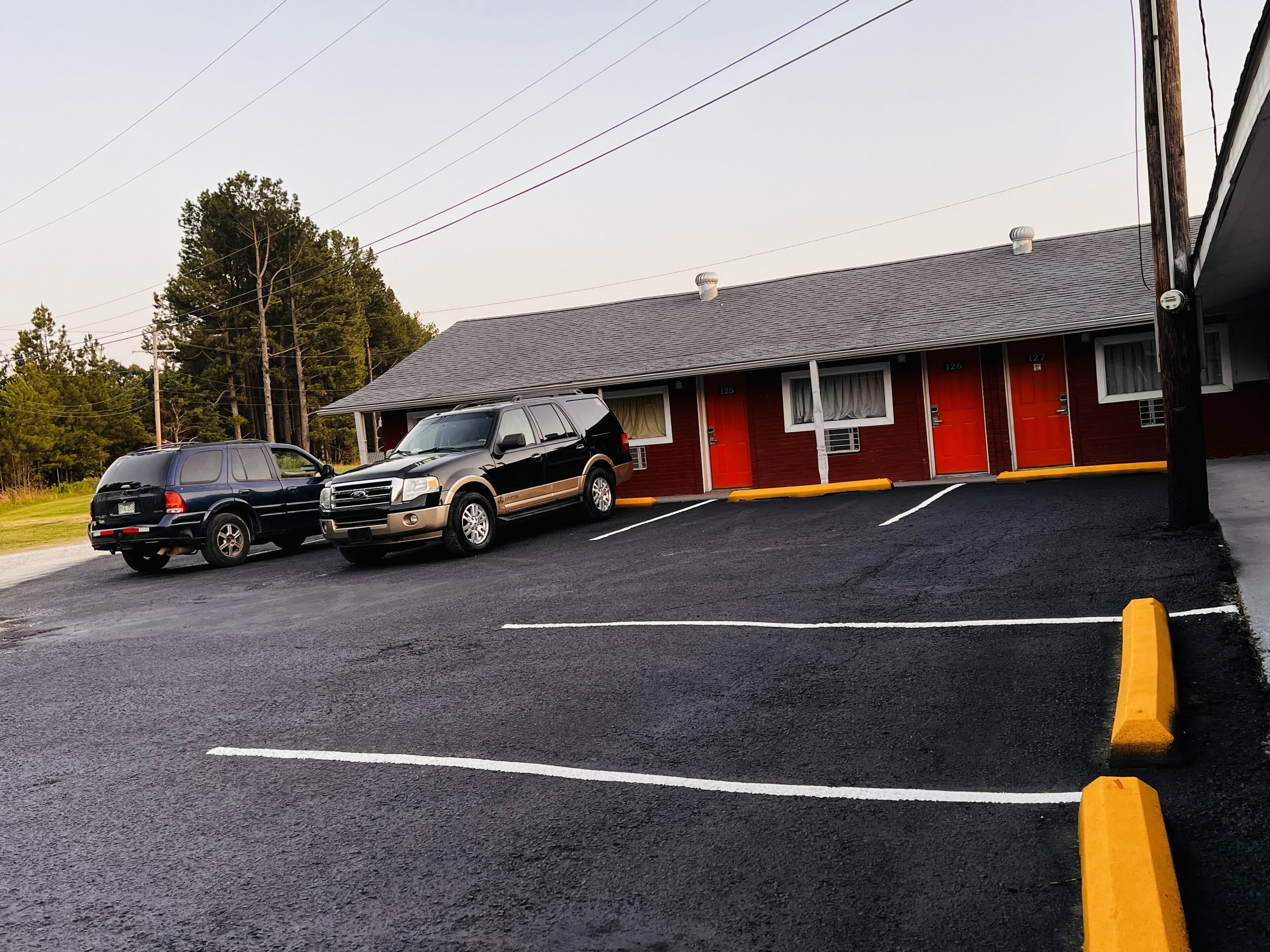 A parking lot with two SUVs parked in front of a building with red doors and a grey roof.