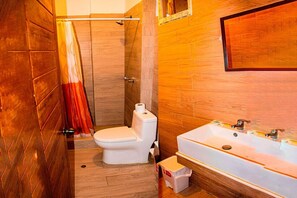 A bathroom with a wooden floor, a white toilet, a shower area, and a sink with a mirror above it. - Hotel Costa Blanca Mancora (Los Organos)