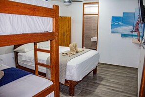A room with bunk beds, a wooden wardrobe, a bathroom with a shower, and a painting of a beach scene. - Hotel Costa Blanca Mancora (Los Organos)
