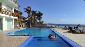 A swimming pool with a wooden deck, palm trees, and a view of the ocean.