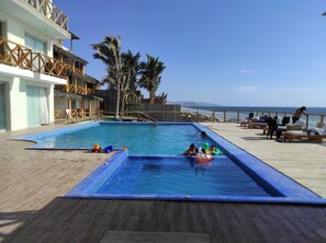 Une piscine avec une terrasse en bois, des palmiers et une vue sur l’océan.