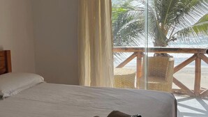 A hotel room with a bed, a window with curtains, a view of palm trees, and a balcony with wicker furniture.