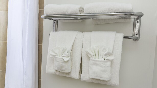 A bathroom with a towel rack holding two folded towels and two towels with folded ends. - Flamingo Express Hotel (Kissimmee)