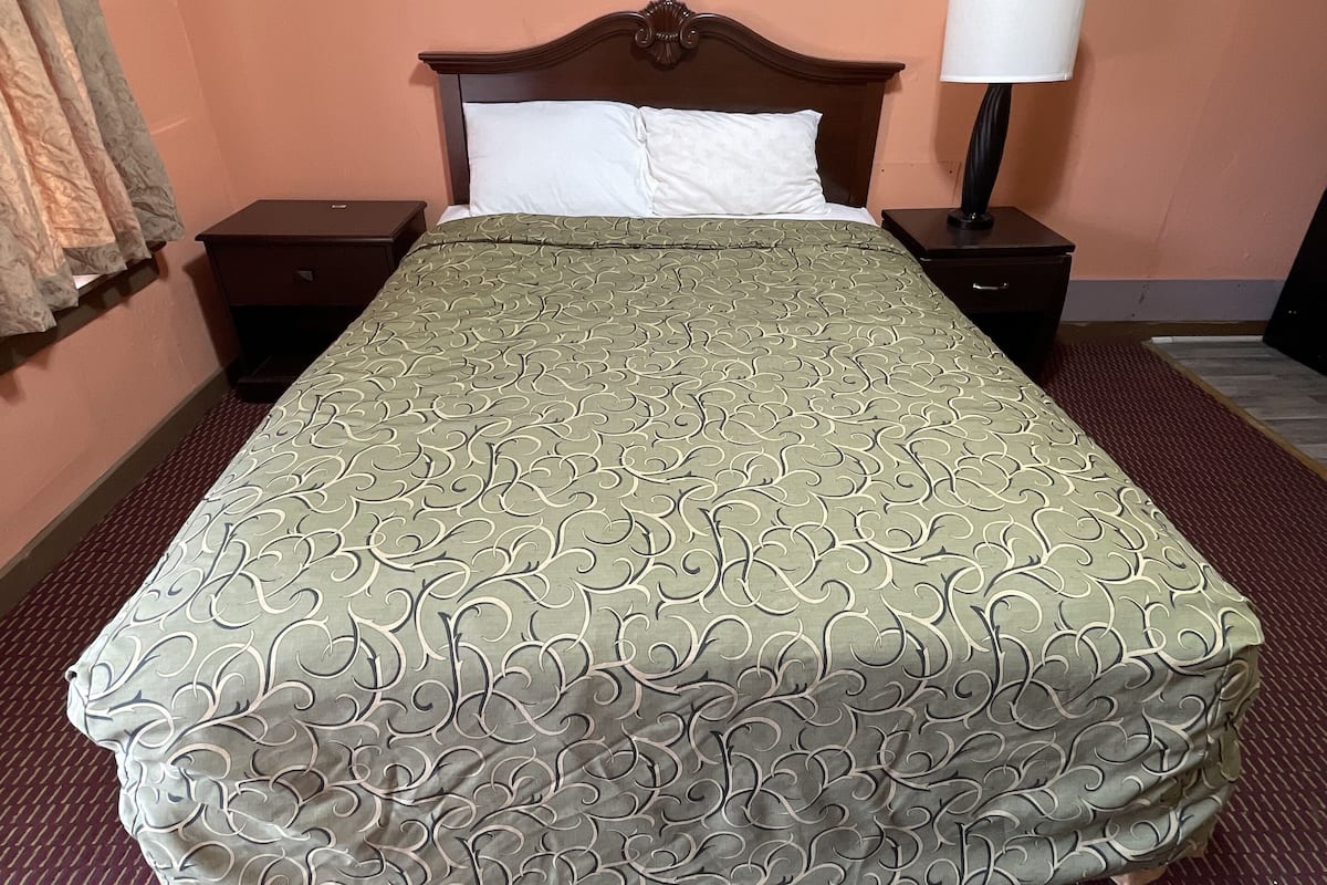 Une chambre d’hôtel avec un lit, une table de chevet, une lampe et une fenêtre avec des rideaux.