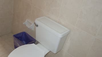 Un baño estándar con inodoro, un bote de basura y paredes con azulejos.