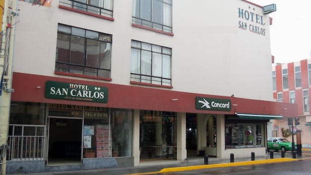 Hotel 'Hotel San Carlos' met een Concord bord, een zichtbare ingang en een straatbeeld met een groene auto geparkeerd voor de deur.