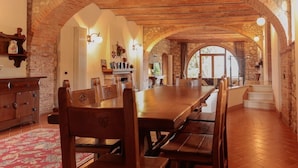 Un comedor con una larga mesa de madera y sillas, paredes de piedra y un tapete rojo con motivos.