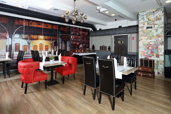 Un restaurante con suelo de madera, sillas tapizadas en rojo y negro, una araña y una pared decorada con papeles.