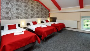 A hotel room with three beds, each with a red bedspread and white pillows, a grey carpet, and a stone-patterned wall. - Przystanek Toruń (Torun)