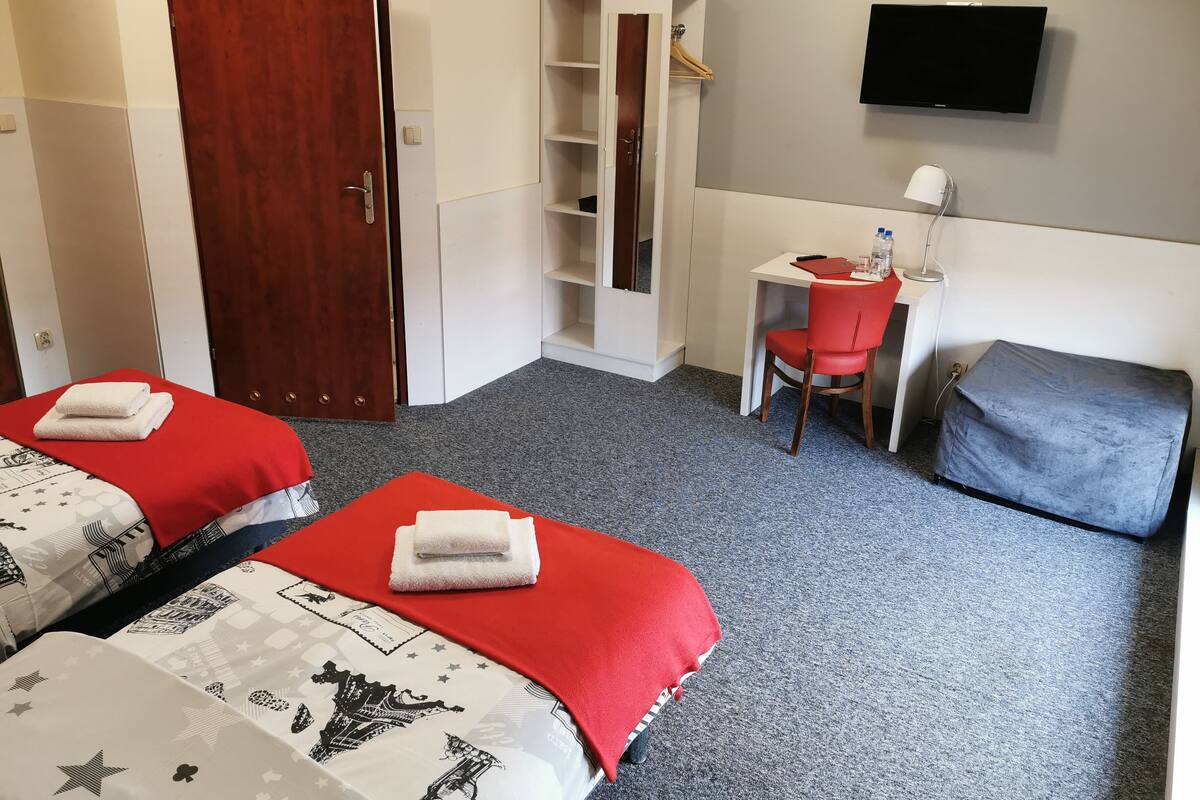 A hotel room with two beds, a desk, a chair, a TV, and a wardrobe.