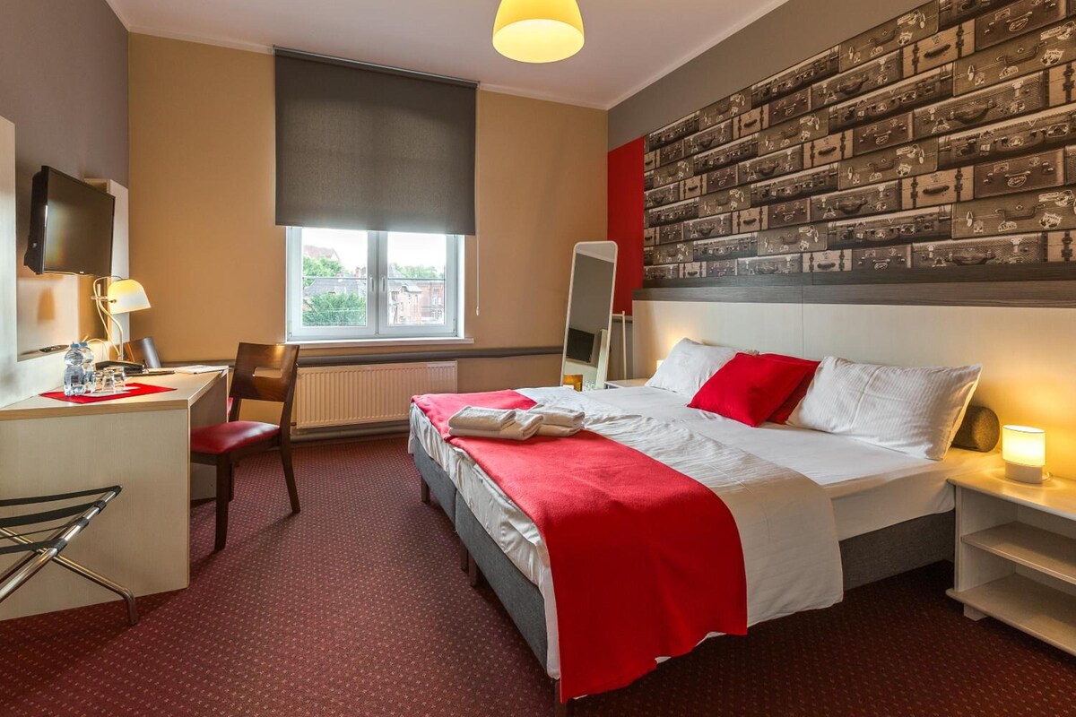 Une chambre d'hôtel équipée d'un lit, d'un bureau, d'une chaise et dont un mur est décoré de vieilles valises.