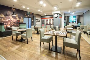 Un restaurante moderno con piso de madera, asientos acolchados color verde y un mural de paisaje urbano.