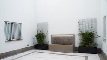 Un espacio interior moderno con suelo de baldosas, una fuente central y dos plantas en macetas.