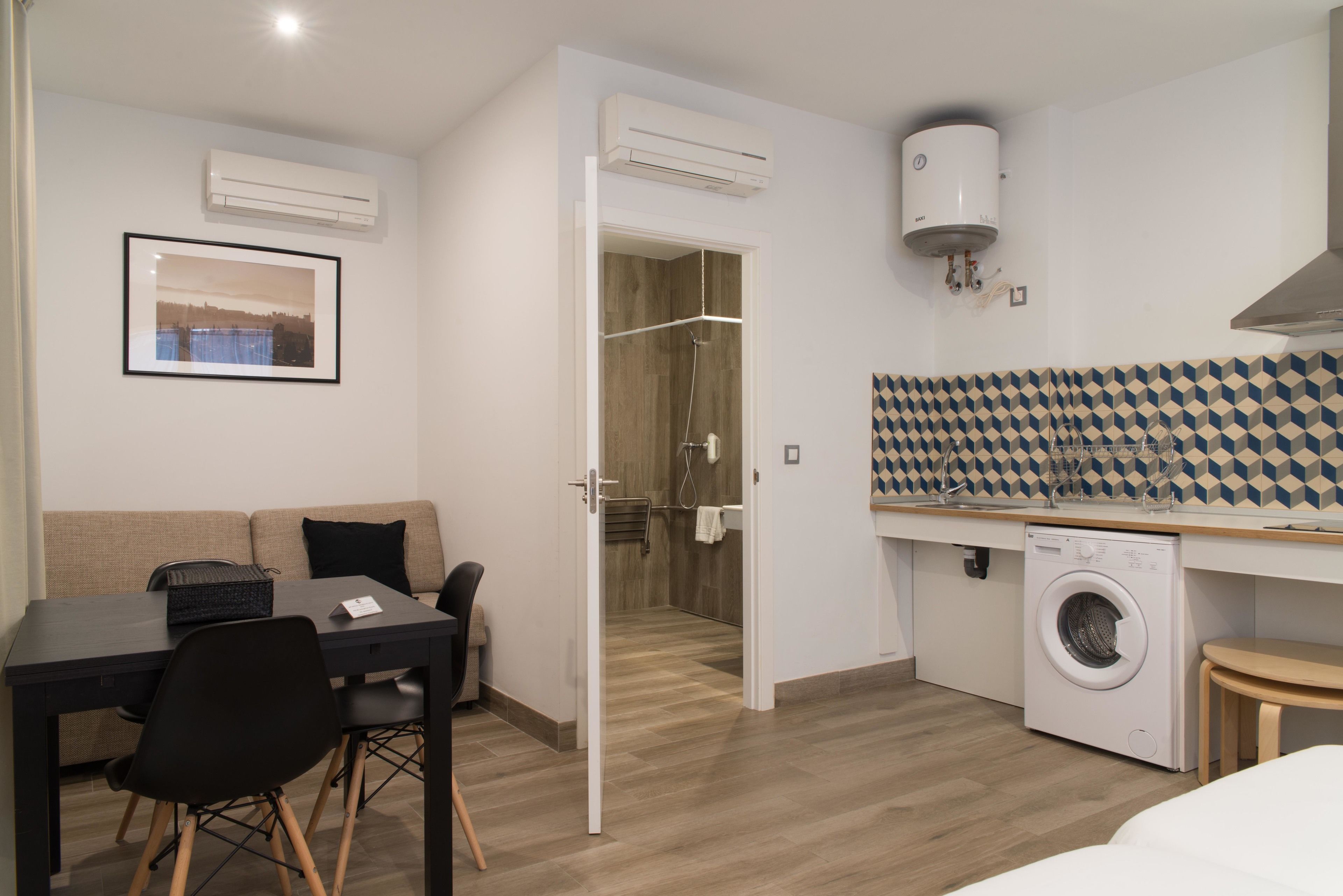 Una habitación de hotel compacta con zona de comedor, lavadora y ducha.