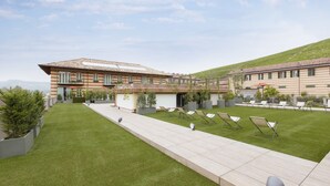 Un edificio moderno con techo plano, ventanas amplias y un césped cuidado con sillones de descanso.