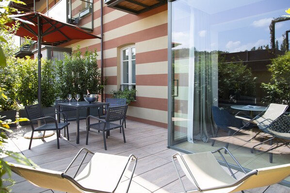 Un patio al aire libre con mesa y sillas, un cerramiento de vidrio y plantas en macetas.