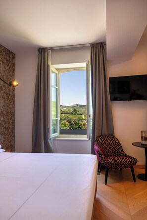 Una habitación de hotel con una cama, una silla, un televisor y un ventanal con cortinas.