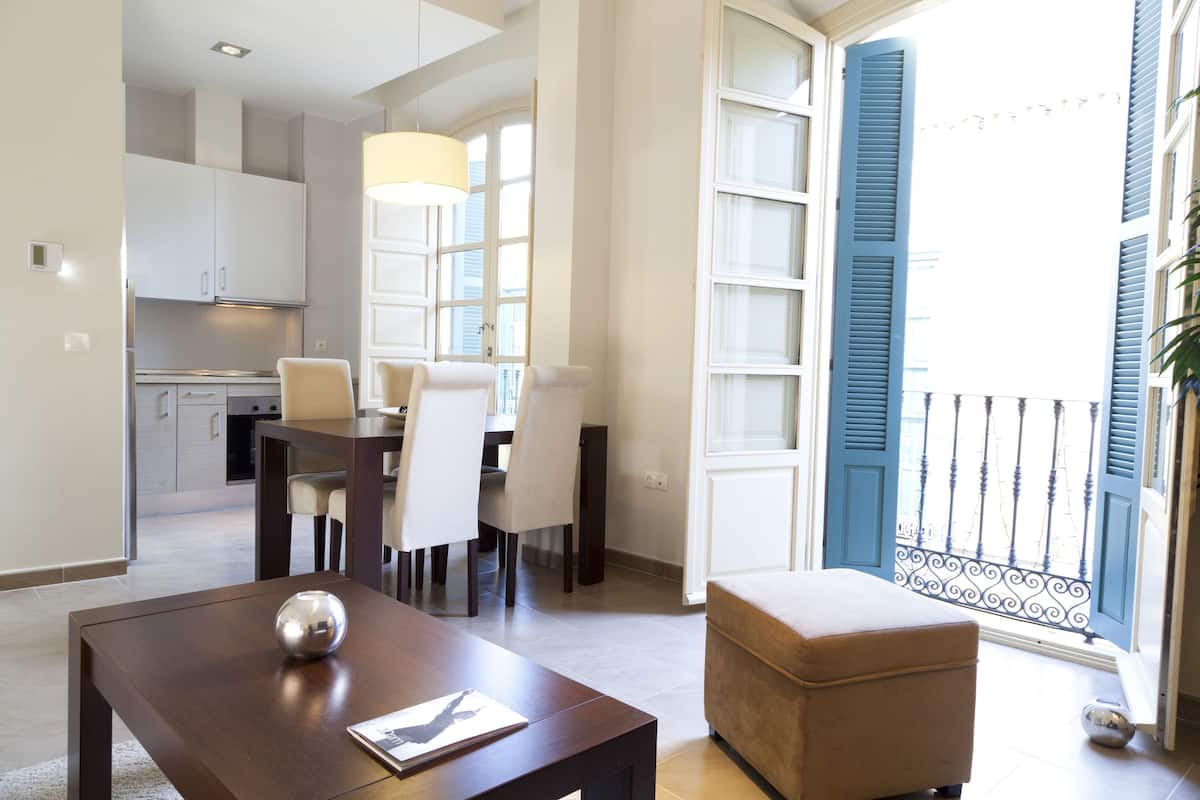 Un salon moderne avec un coin repas, une cuisine à l’arrière-plan et un balcon avec des volets bleus.