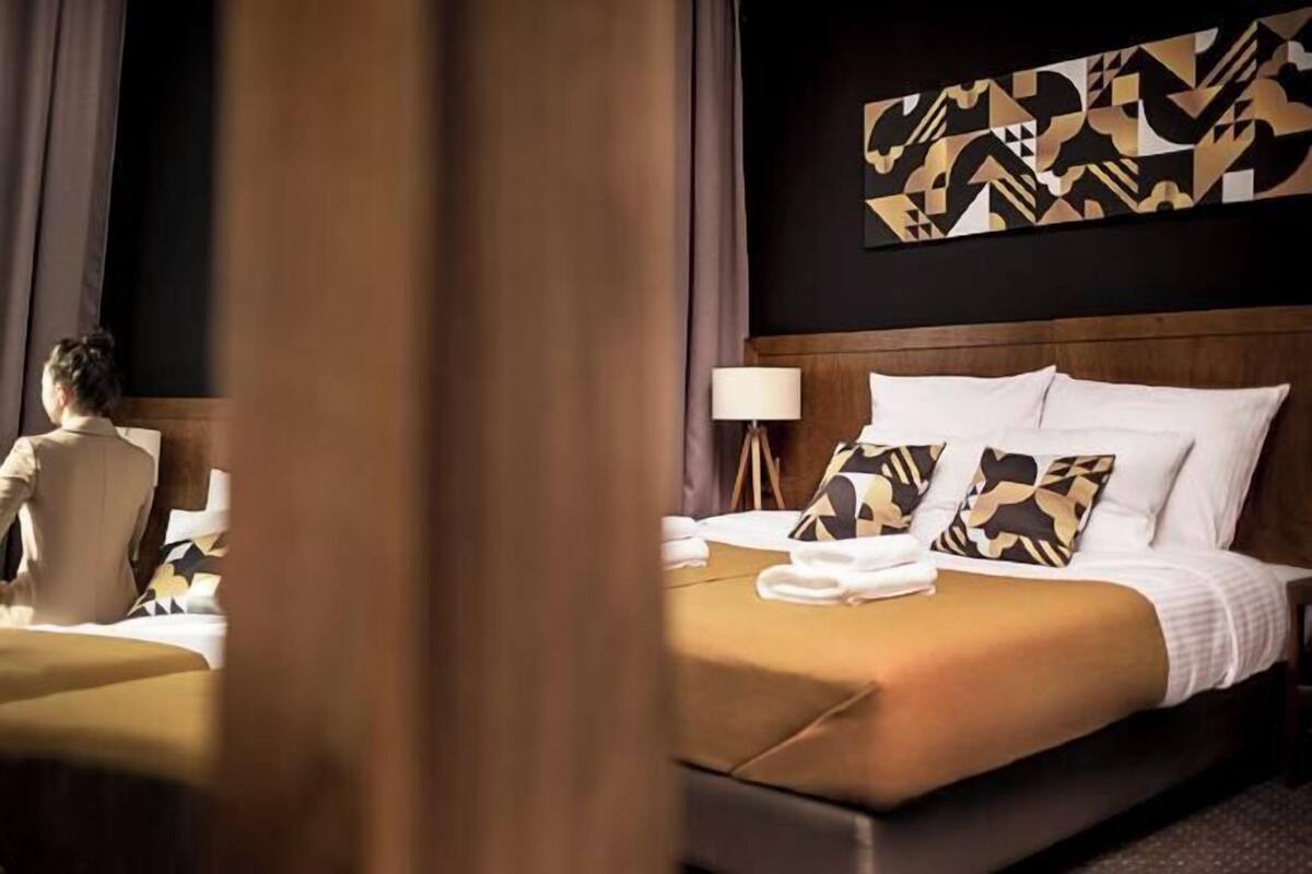 A hotel room with a bed, pillows, a lamp, and a wall art piece.