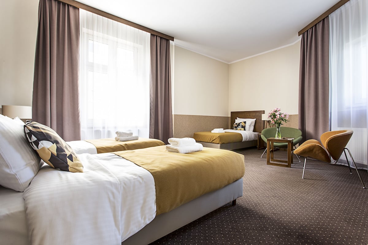 A hotel room with two beds, a sitting area with a chair and table, and a view of the outdoors.