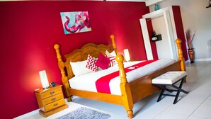 A bedroom with a wooden four-poster bed, a nightstand with a lamp, a bedside table, and a blue rug. - Casa Tamar Guest Apartments (Kingston)