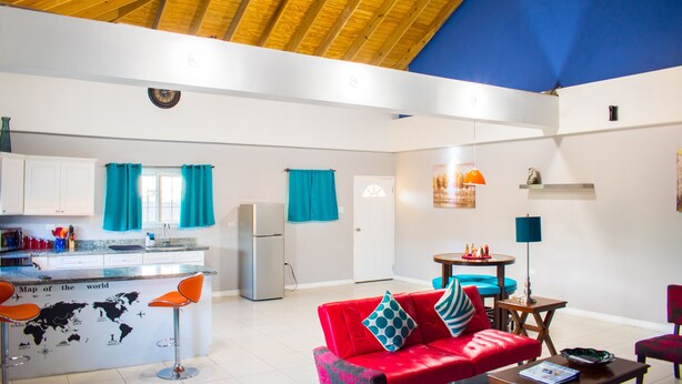 A spacious living area with a red sofa, a kitchen with a fridge, and a dining area with a table and chairs. - Casa Tamar Guest Apartments (Kingston)