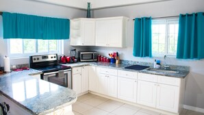 A kitchen with white cabinets, a granite countertop, a stove, a microwave, and a sink. - Casa Tamar Guest Apartments (Kingston)