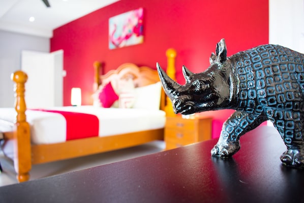 A room with a bed, a red wall, and a decorative rhinoceros figurine on a table. - Casa Tamar Guest Apartments (Kingston)