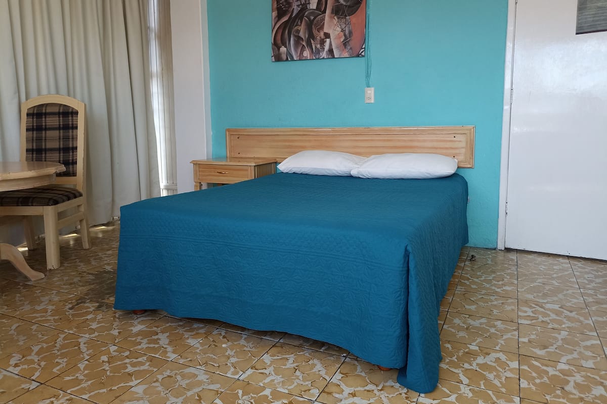 A bedroom with a bed, a chair, a nightstand, and a painting on the wall.