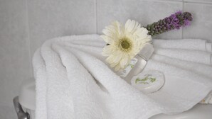 A bathroom with a white towel, a white flower, and a small bottle on the toilet.