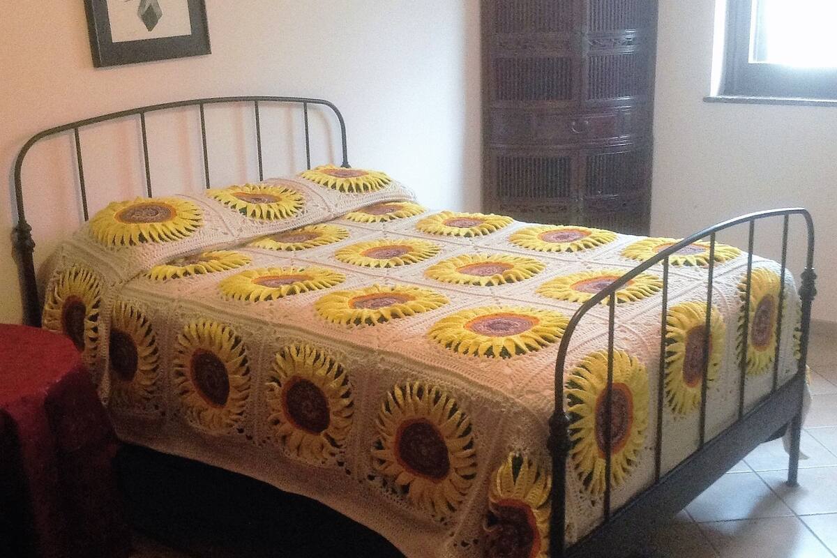 Una cama con estructura metálica y colcha estampada con motivos de girasoles.
