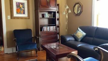 A living room with a dark blue armchair, a wooden coffee table, a leather sofa, and a bookshelf filled with books.