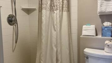 A bathroom with a shower curtain, a toilet, and a shelf with toiletries.