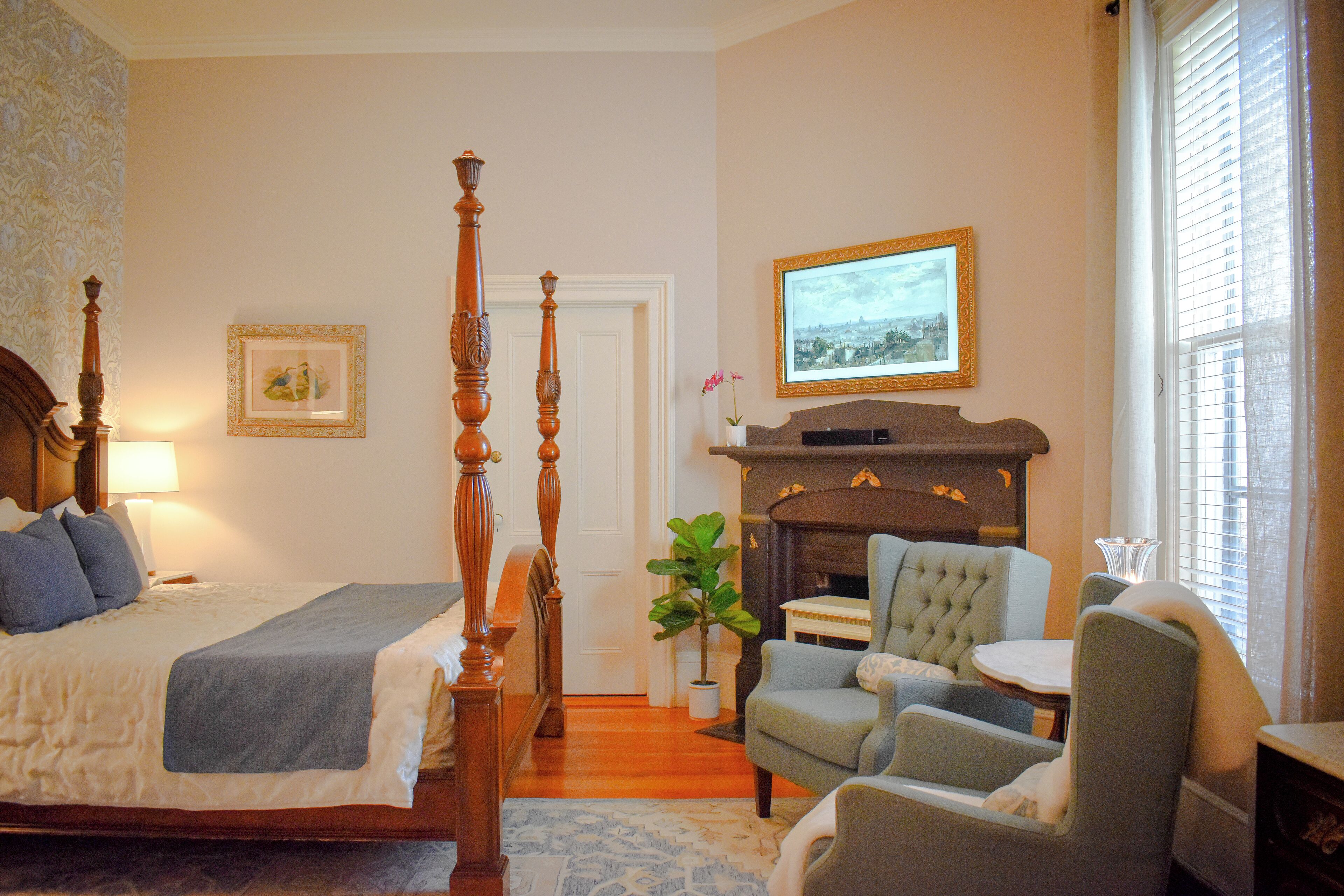 Un dormitorio con cama con dosel, una chimenea, una zona de estar con una silla y una mesa, y un cuadro en la pared.