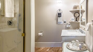 Un baño con ducha, lavabo, espejo y tocador con artículos de aseo.