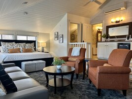 Una habitación de hotel con cama, sofá, sillón, una mesita y una zona de cocina.