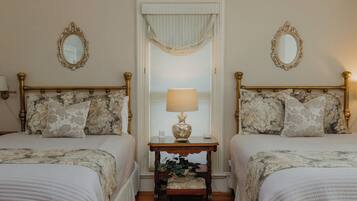 A double room with two beds, each with a floral-patterned headboard, a bedside table with a lamp, and a mirror on the wall.