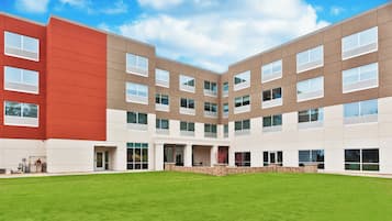 Un edificio moderno con techo plano, ventanas amplias y un patio central con césped cuidado.