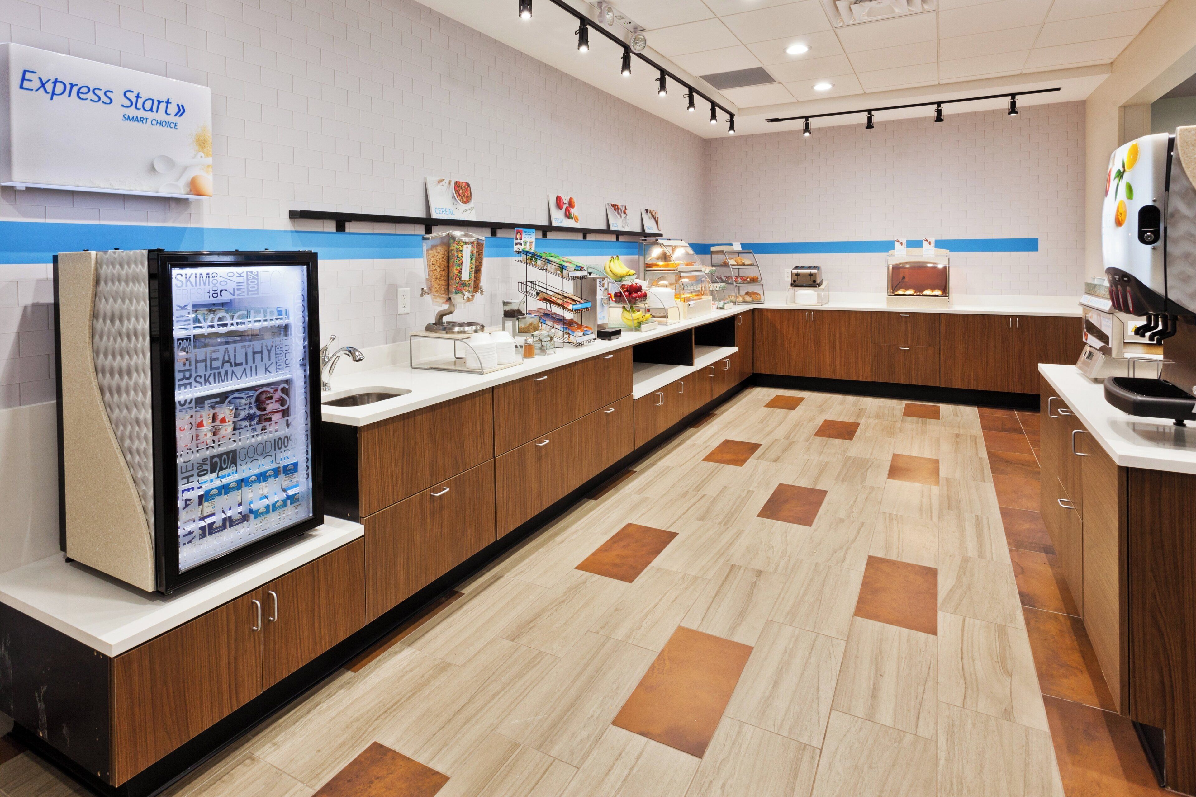 A modern breakfast area with a refrigerator, cereal, fruit, and a coffee machine.