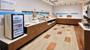 A modern breakfast area with a refrigerator, cereal, fruit, and a coffee machine.