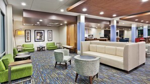 Un hall d’hôtel avec des fauteuils verts, un canapé beige et une moquette à motifs.
