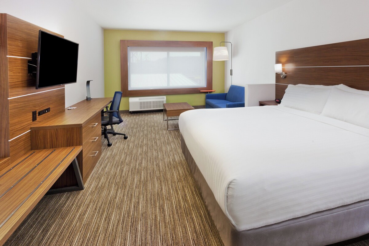 Une chambre d’hôtel comprenant un lit, un bureau avec un téléviseur à écran plat, une chaise, une petite table et une fenêtre.