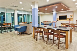 Un espace repas moderne avec des tables et des chaises en bois, un banc à motifs et un grand écran mural.