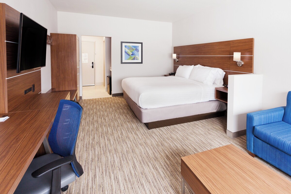 Une chambre d’hôtel avec un lit, un bureau, une chaise, une télévision et un canapé bleu.