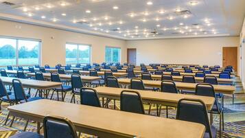 Un salón de conferencias con varias mesas y sillas, ventanas amplias y piso alfombrado.