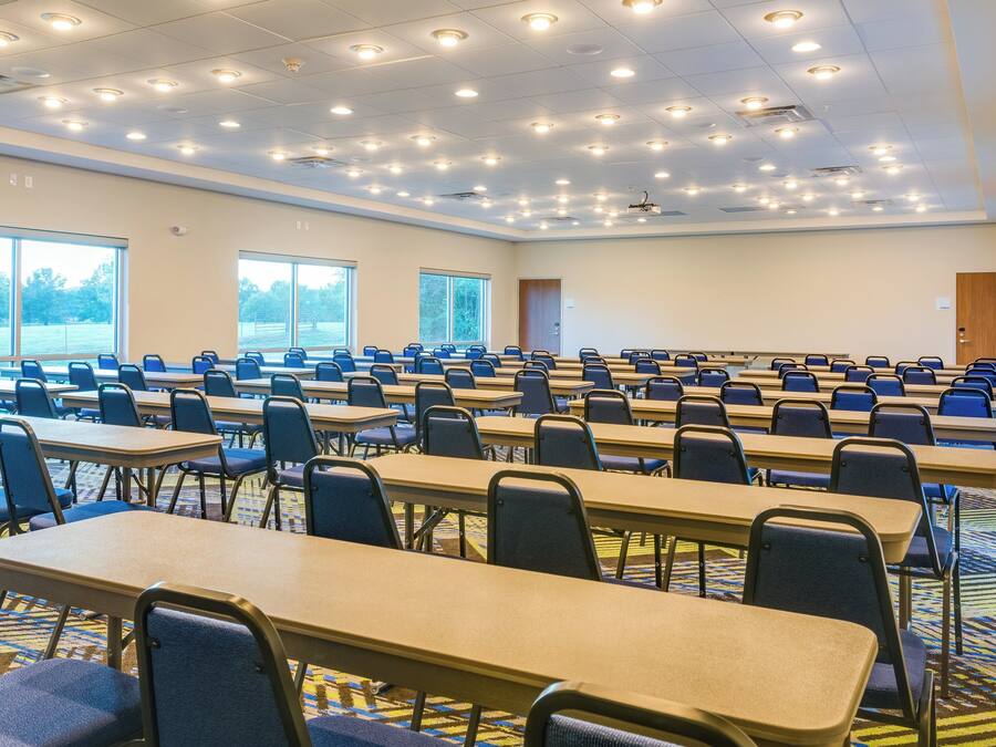A conference room with multiple tables and chairs, large windows, and a carpeted floor.