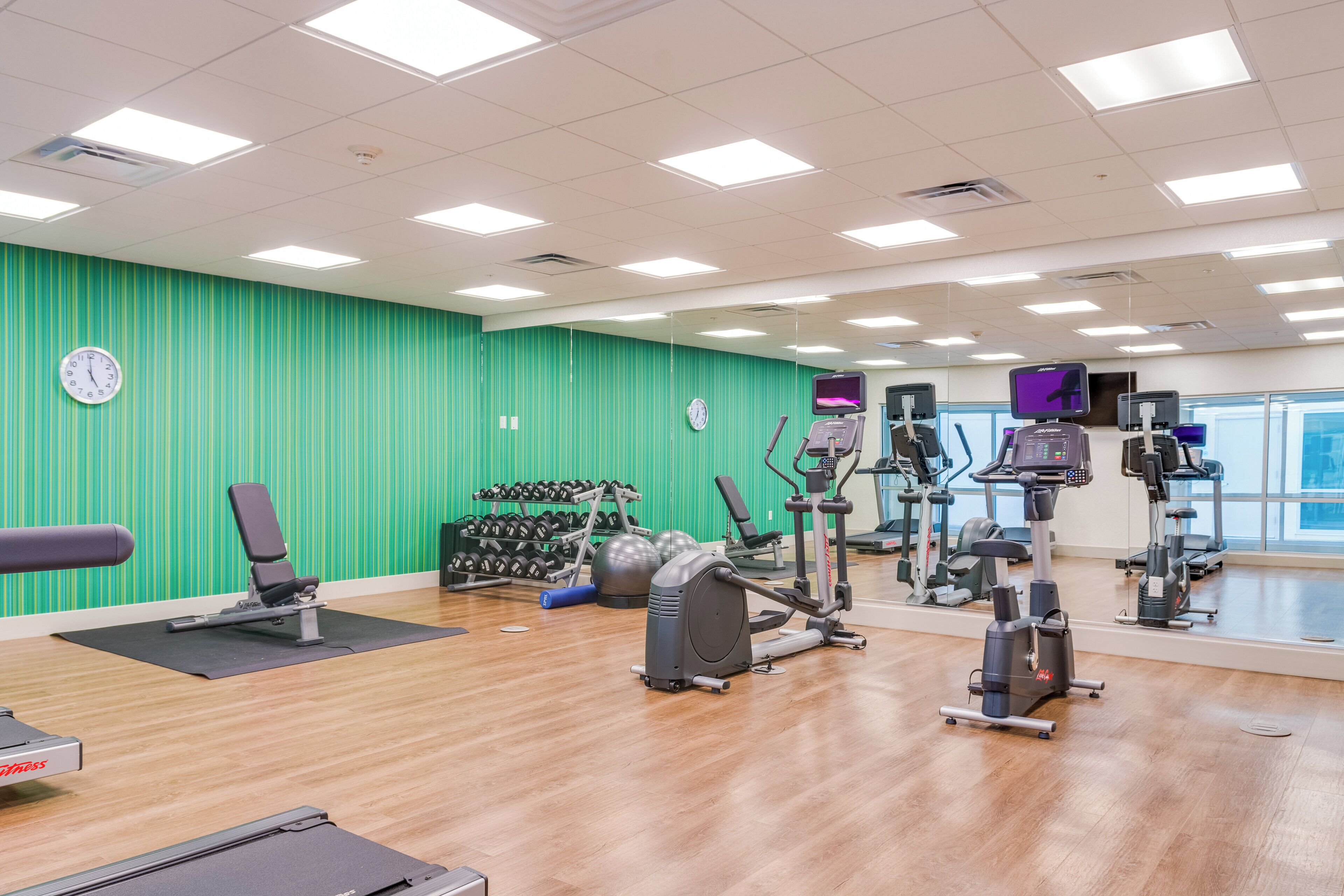 Un gimnasio con diferentes equipos de ejercicio, un reloj y una pared verde.