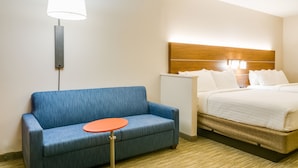 Ein Hotelzimmer mit einem blauen Sofa, einem kleinen orangefarbenen Tisch, einem Bett mit weißer Bettwäsche und einer Wandlampe.