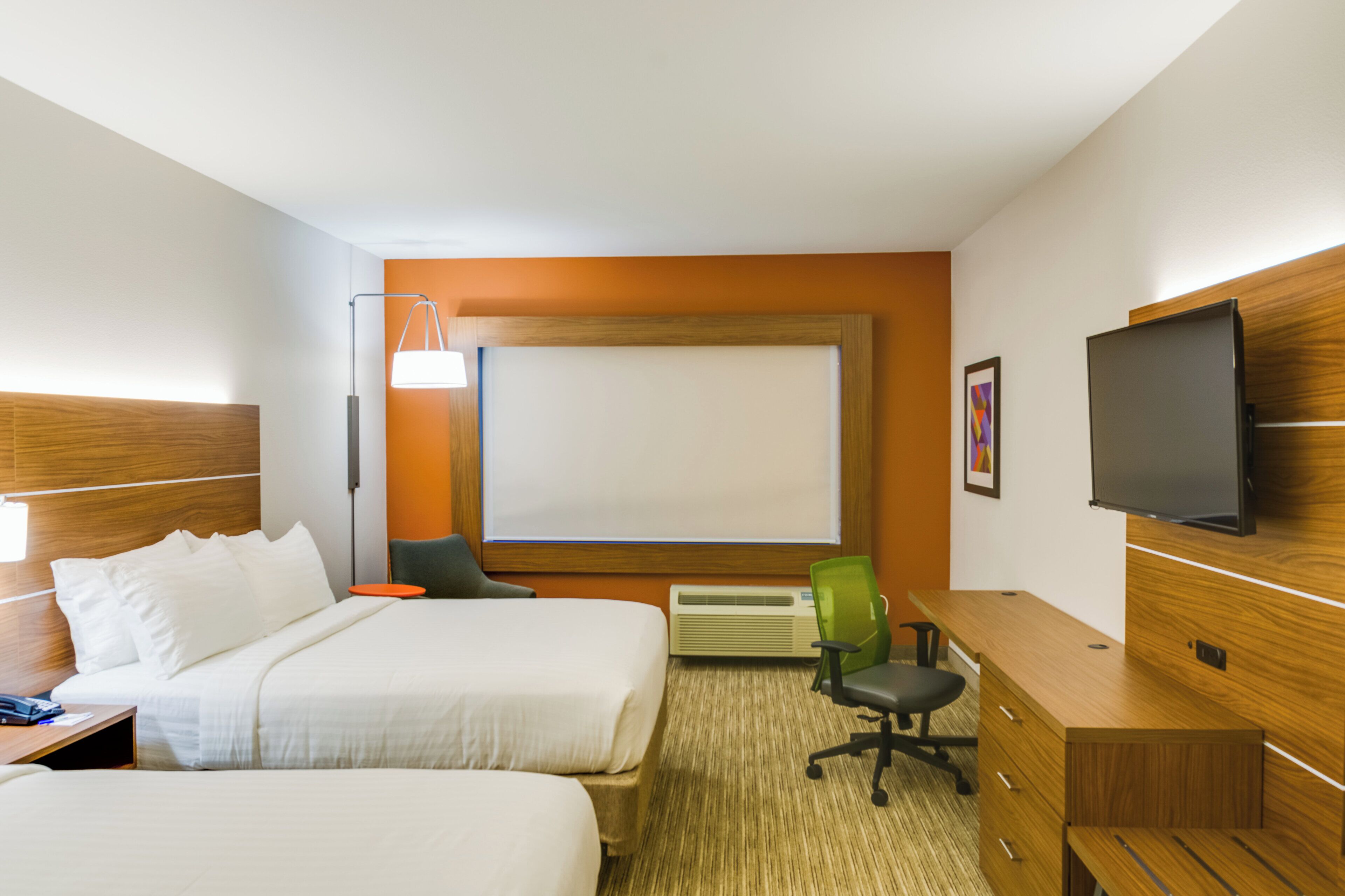 Habitación de hotel con dos camas, un escritorio, una silla, un televisor de pantalla plana, un ventanal grande y un aire acondicionado instalado en la pared.