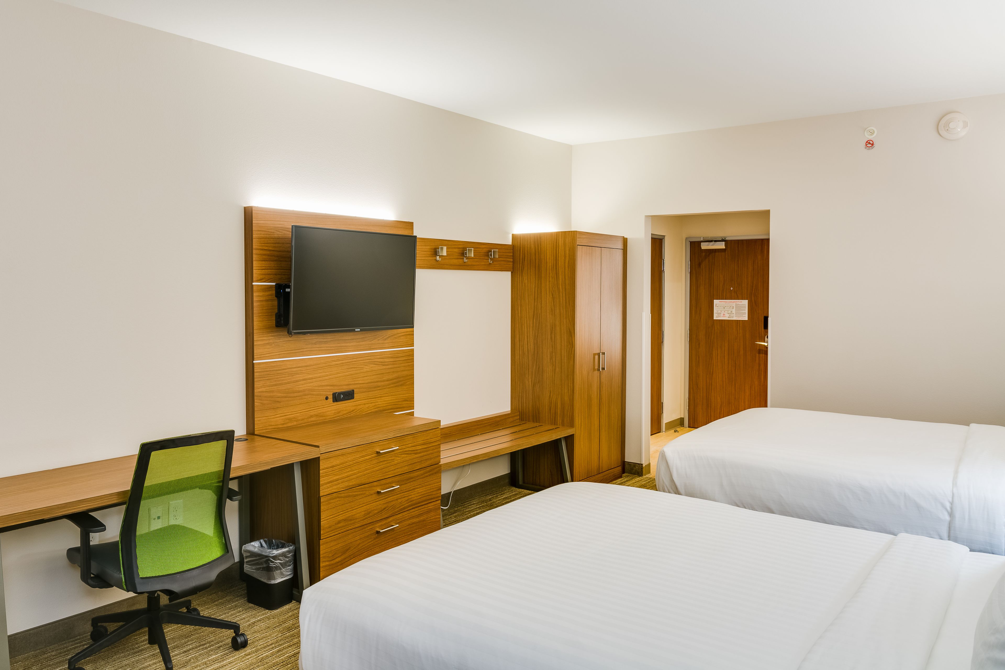 A hotel room with a wooden desk, a television, a green office chair, two beds, and a trash bin.